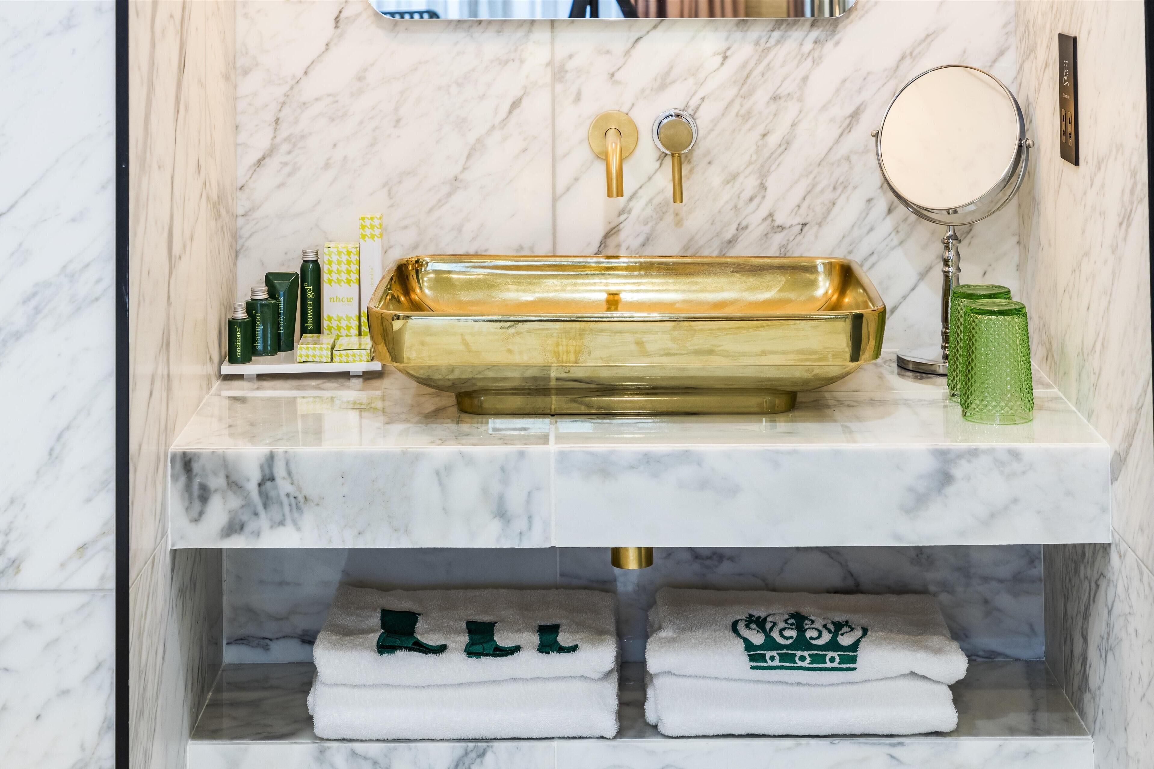 A bathroom with a marble wall, a gold sink, and a mirror.