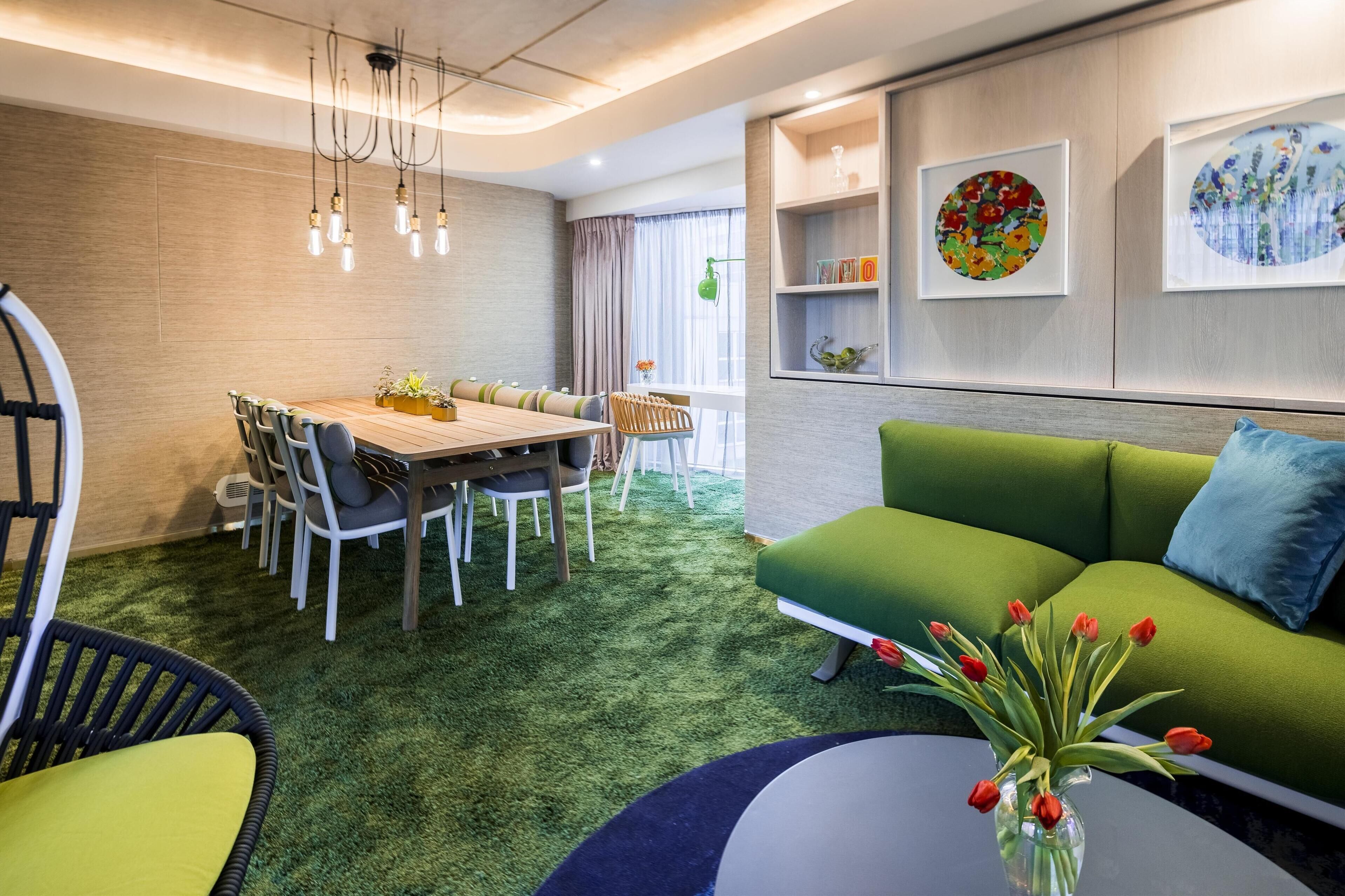 A modern living room with a green sofa, a dining table with chairs, and a coffee table with a vase of tulips.