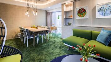 A modern living room with a green sofa, a dining table with chairs, and a coffee table with a vase of tulips.