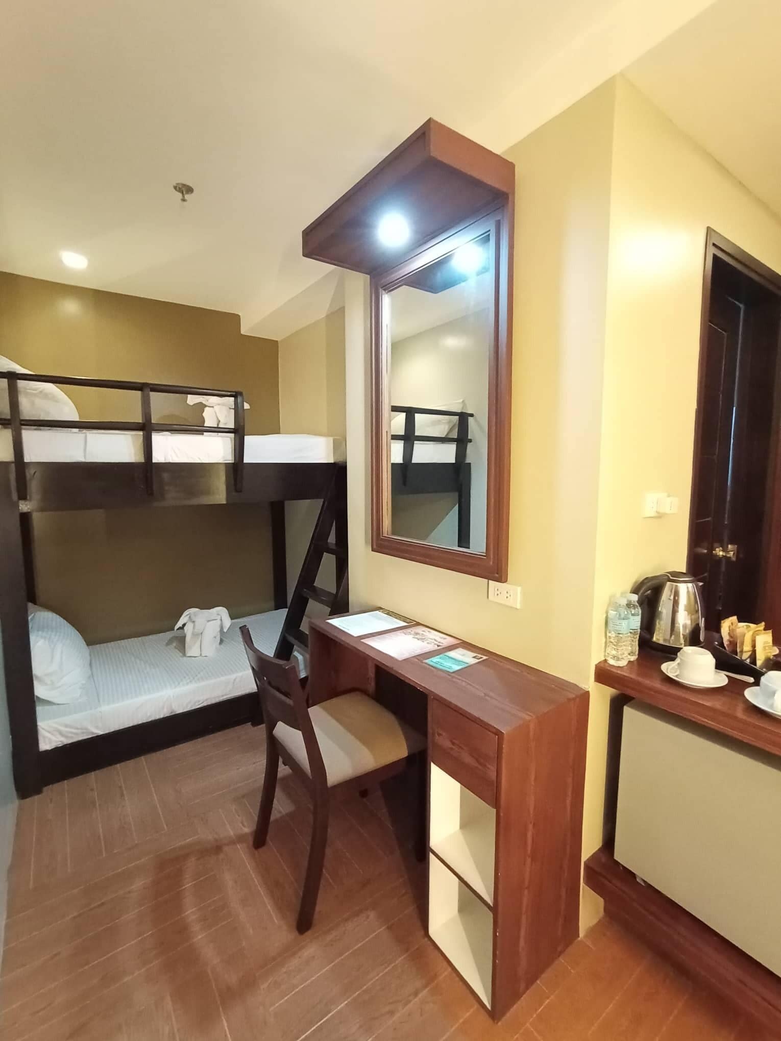 A bunk bed with a desk and chair, a mirror, and a small kitchenette with a kettle and cups.