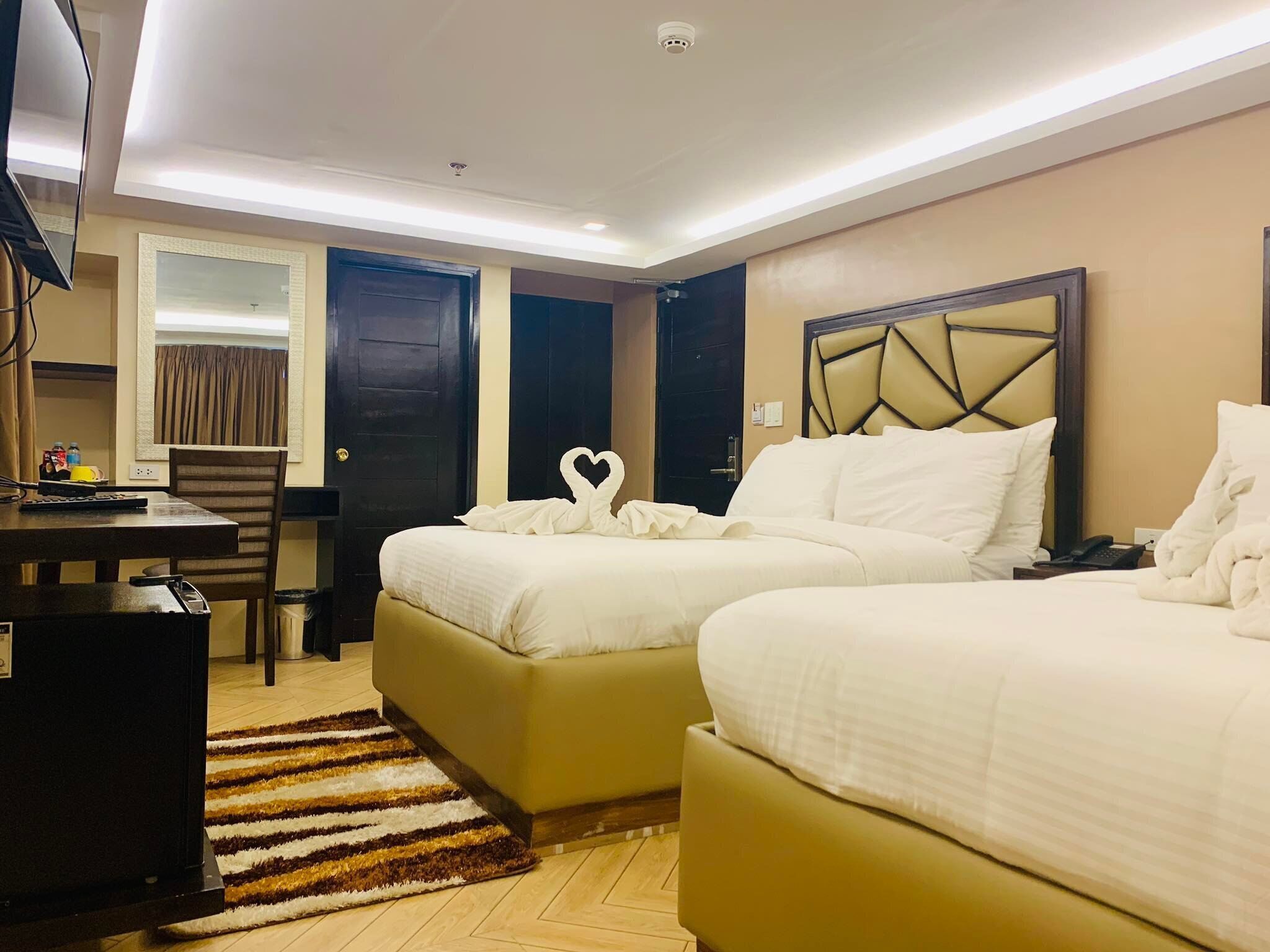 A hotel room with two beds, a desk, a chair, and a TV.