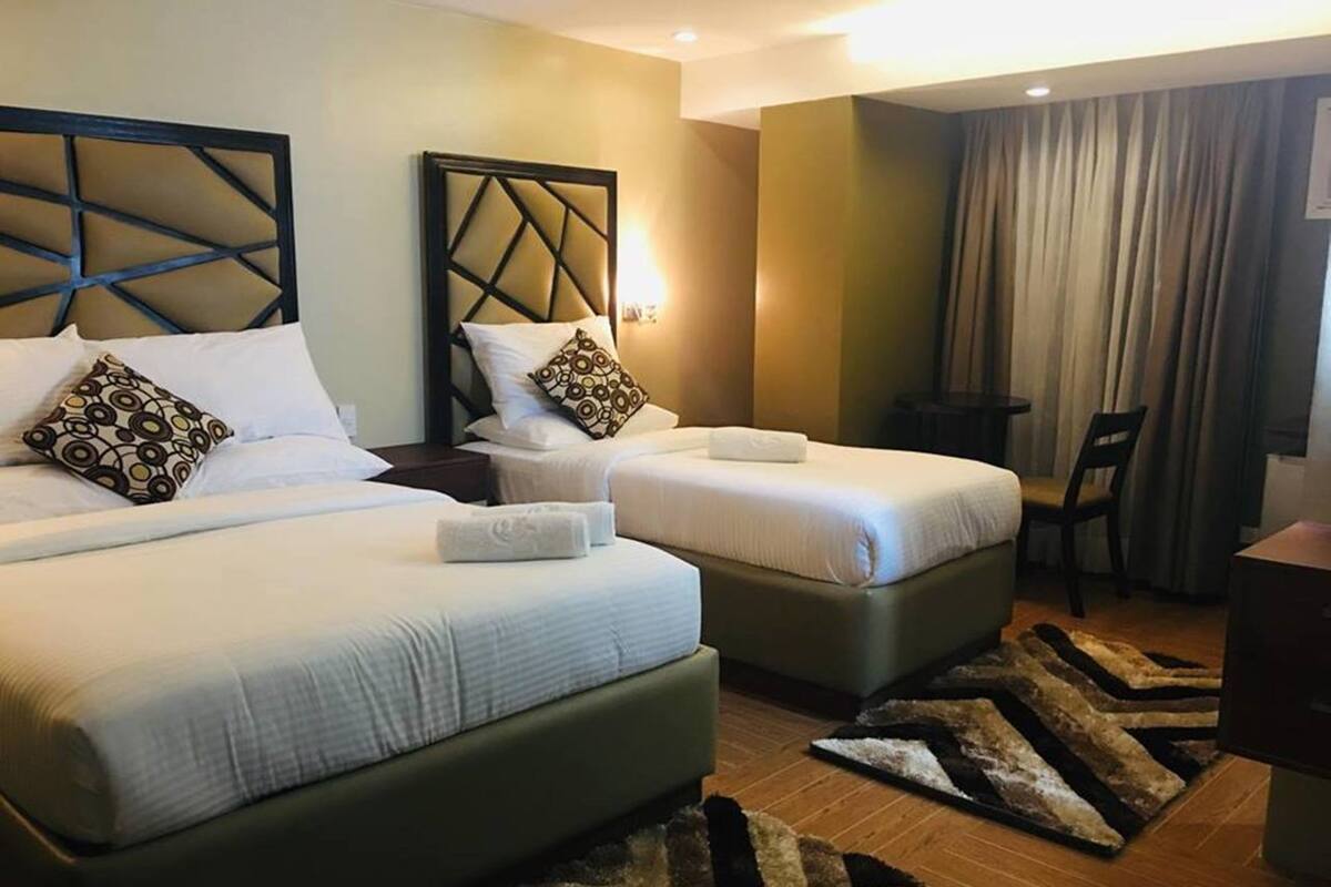 A hotel room with two beds, a small table, a chair, and a large window with curtains.