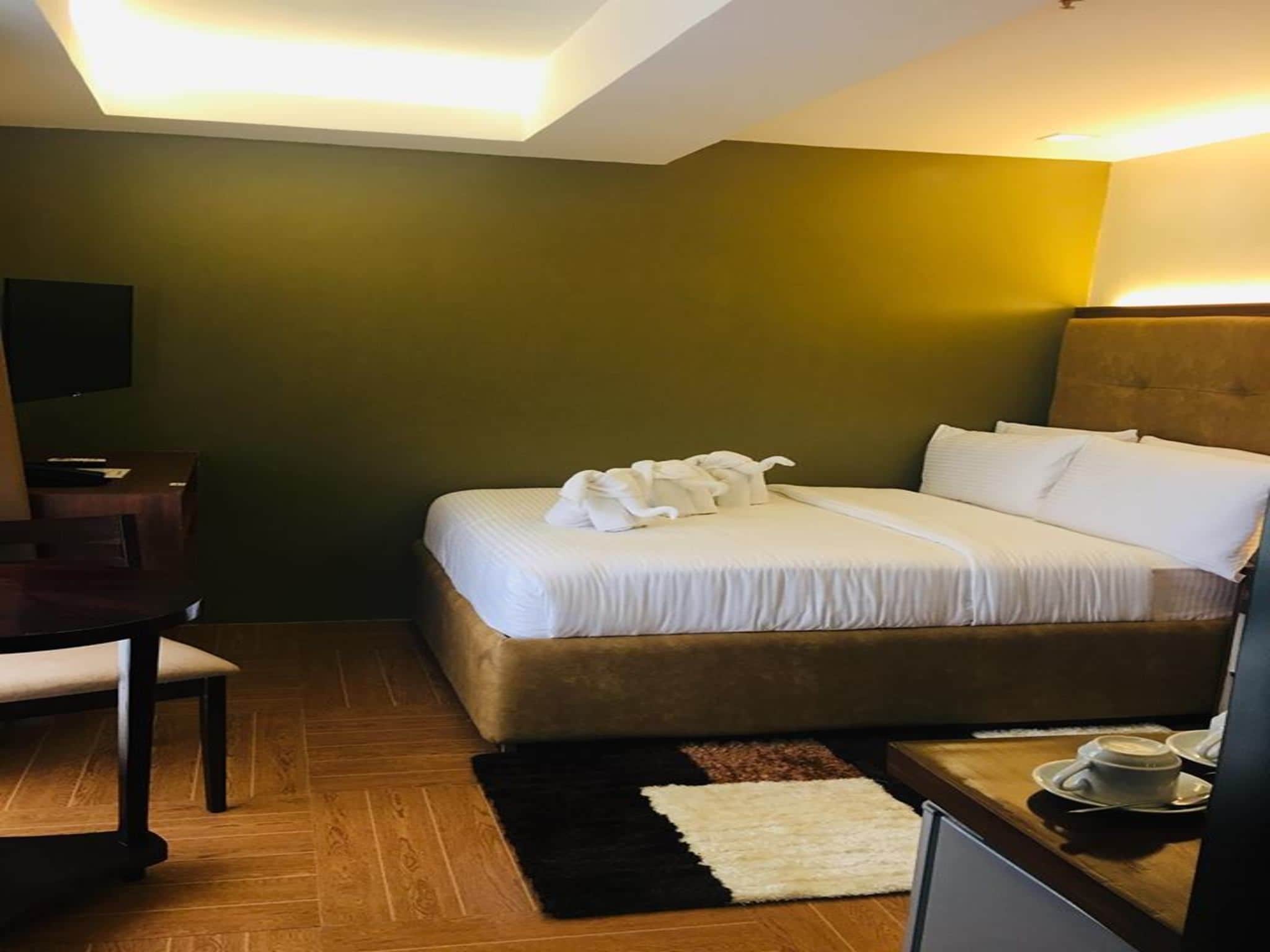 A hotel room with a bed, a desk, a chair, a TV, and a coffee table with cups.