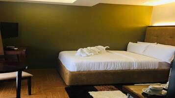 A hotel room with a bed, a desk, a chair, a TV, and a coffee table with cups.
