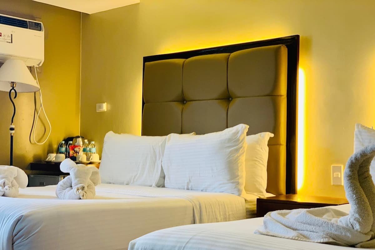 A hotel room with two beds, a bedside table with toiletries, and a wall-mounted air conditioner.