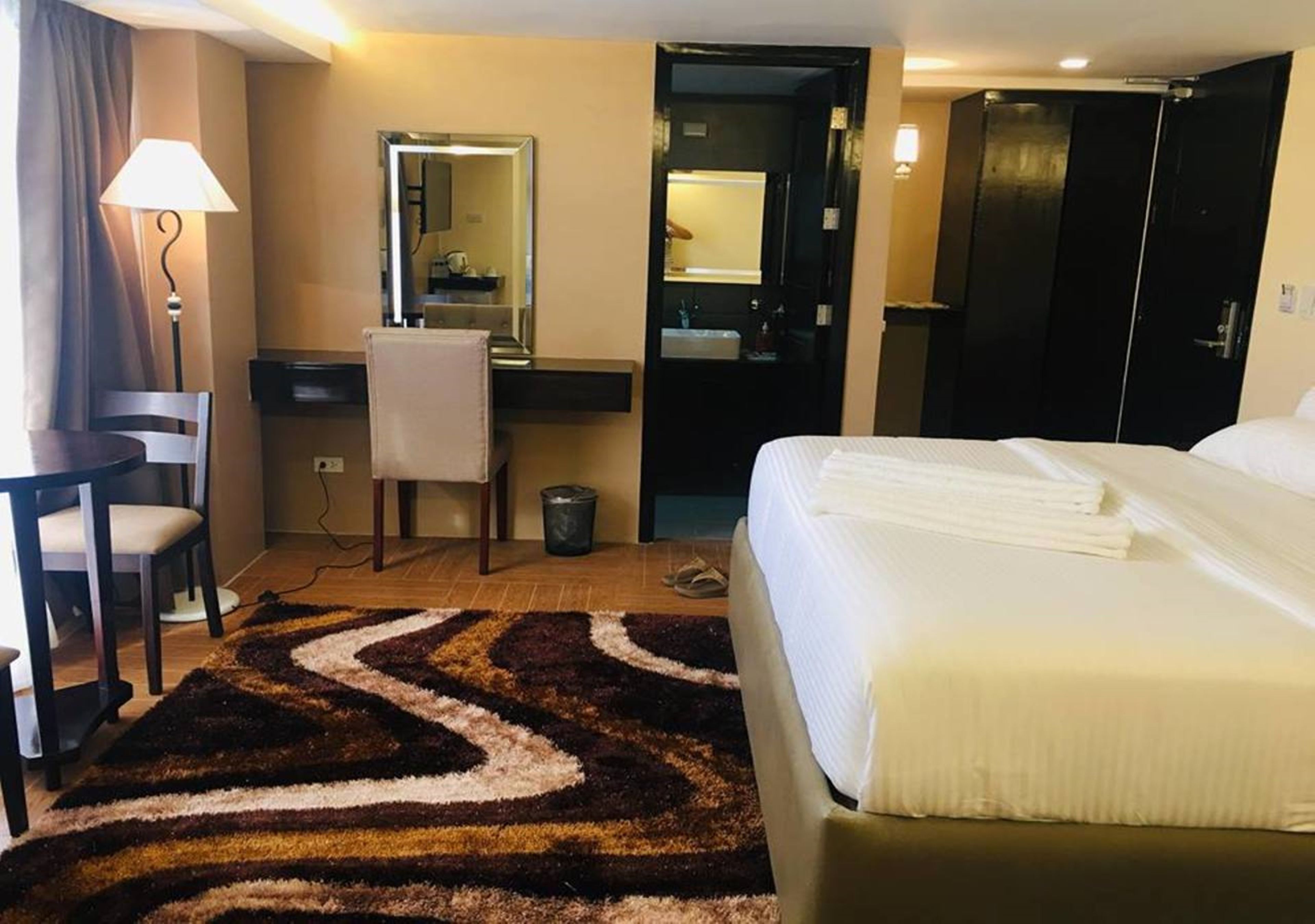A hotel room with a bed, a desk with a chair, a mirror, a wardrobe, and a bathroom door.