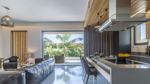 A modern kitchen with a central island, a dining area with a sofa, and a view of greenery outside. - Sofia Luxury Residence (Paphos)