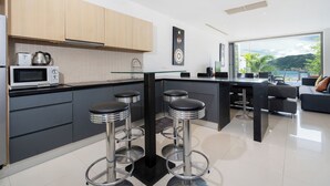 A modern kitchen with a central island, bar stools, and a view of the outdoors. - Villa 3 oceanfront pool villa (Tambon Patong)