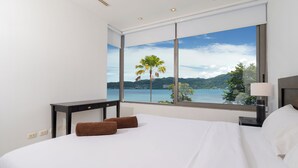 A hotel room with a large window offering a scenic view of a lake and mountains. - Villa 3 oceanfront pool villa (Tambon Patong)