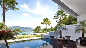 A modern outdoor pool area with a dining table and chairs, surrounded by palm trees and a view of distant mountains. - Villa 0. oceanfront pool villa (Patong)