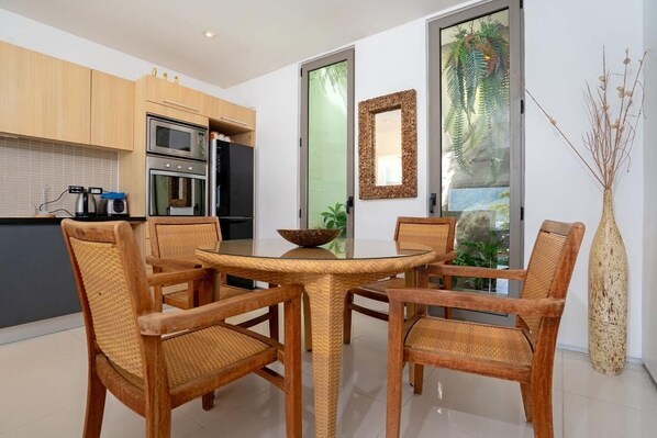A modern kitchen with wooden cabinets, a dining area with wicker chairs, and a large window with a view of greenery.