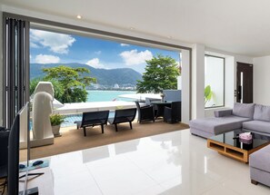A modern living room with a large window overlooking a pool and mountains. There is a sofa, a coffee table, and a desk with a chair.