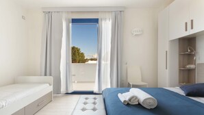 Een moderne slaapkamer met een bed, een bankje, een kledingkast en uitzicht op het groen.