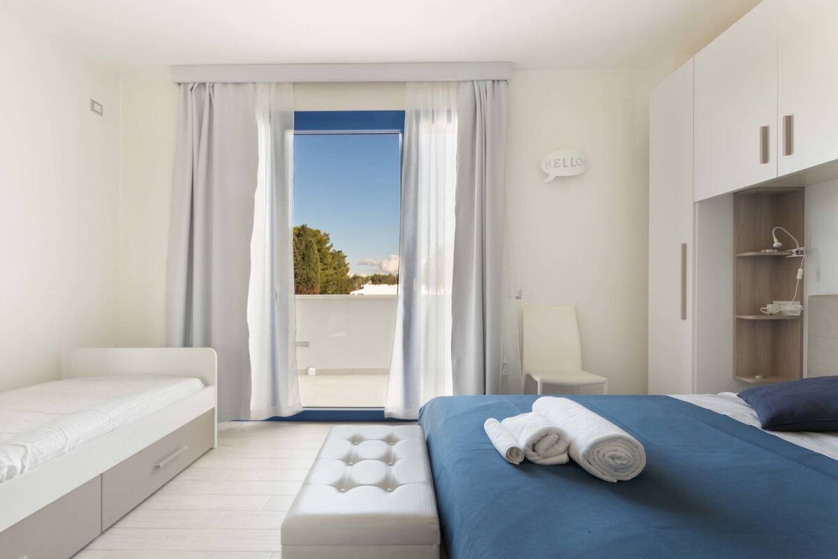 Ein modernes Schlafzimmer mit Bett, Sitzbank, Kleiderschrank und Blick ins Freie.