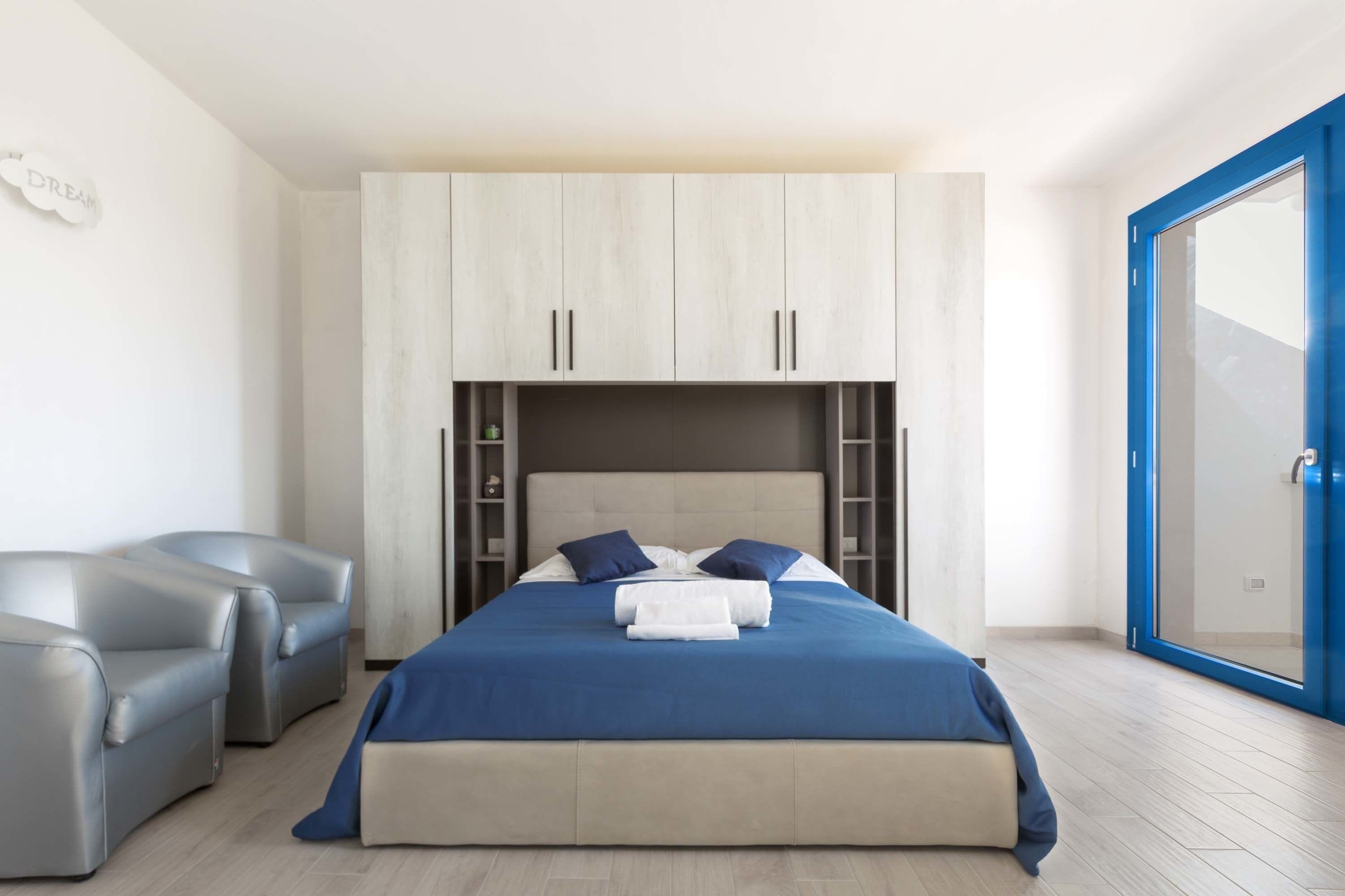 A modern bedroom with a bed, two sofas, a wardrobe, and a sliding glass door.