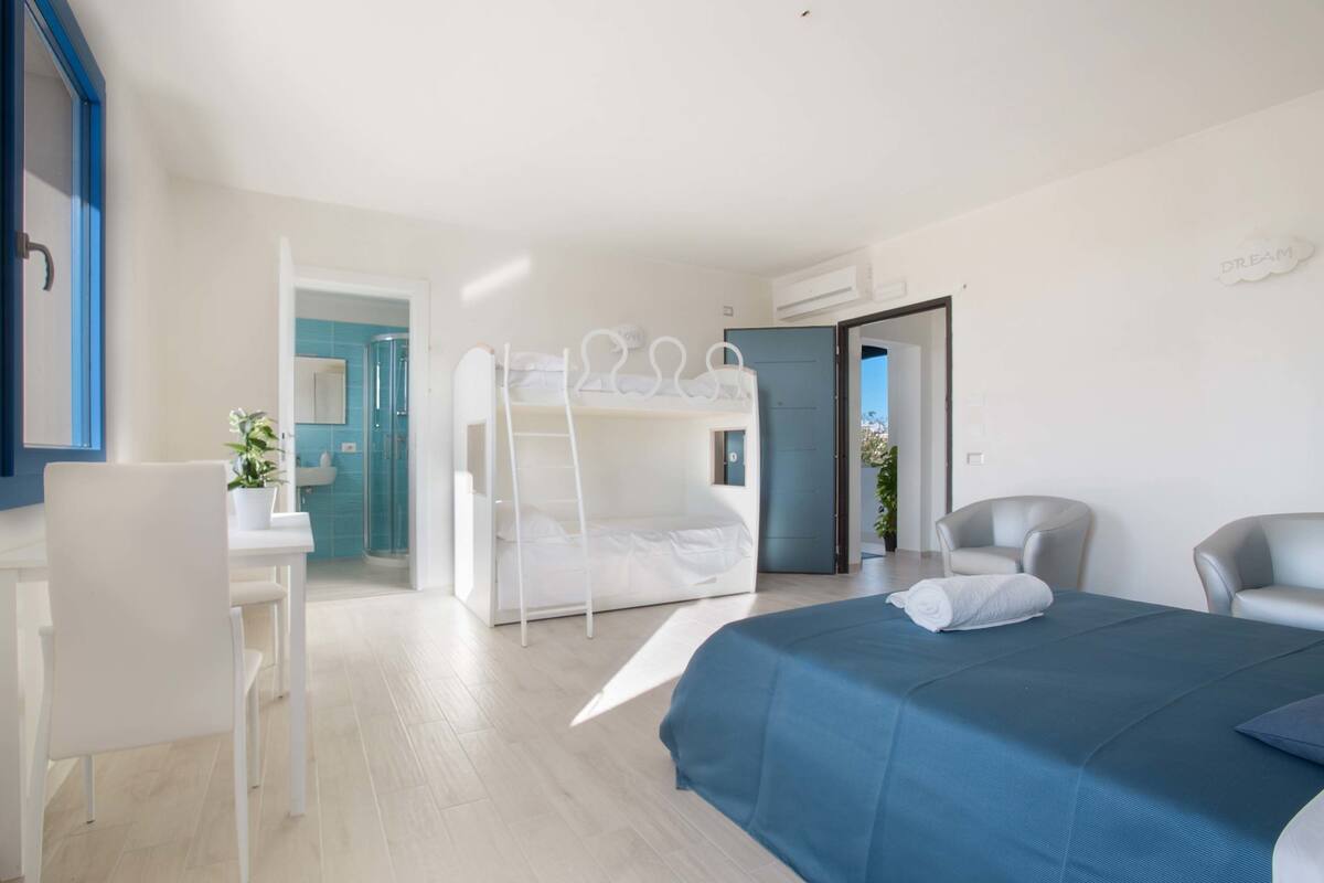 Ein modernes Hotelzimmer mit Etagenbett, Schreibtisch mit Stuhl, Badezimmer mit blauen Fliesen und Blick auf die Stadt.