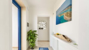 Een hal met een deur met blauwe lijst, een potplant, een kamerkleed met dessin, een wandeling van spiegels en een schilderij van een kustlandschap.