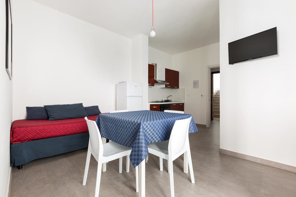 A compact living space with a dining area, a kitchenette, and a bed.