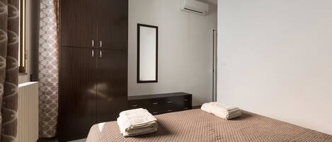 A bedroom with a bed, a wardrobe, a mirror, and an air conditioning unit.