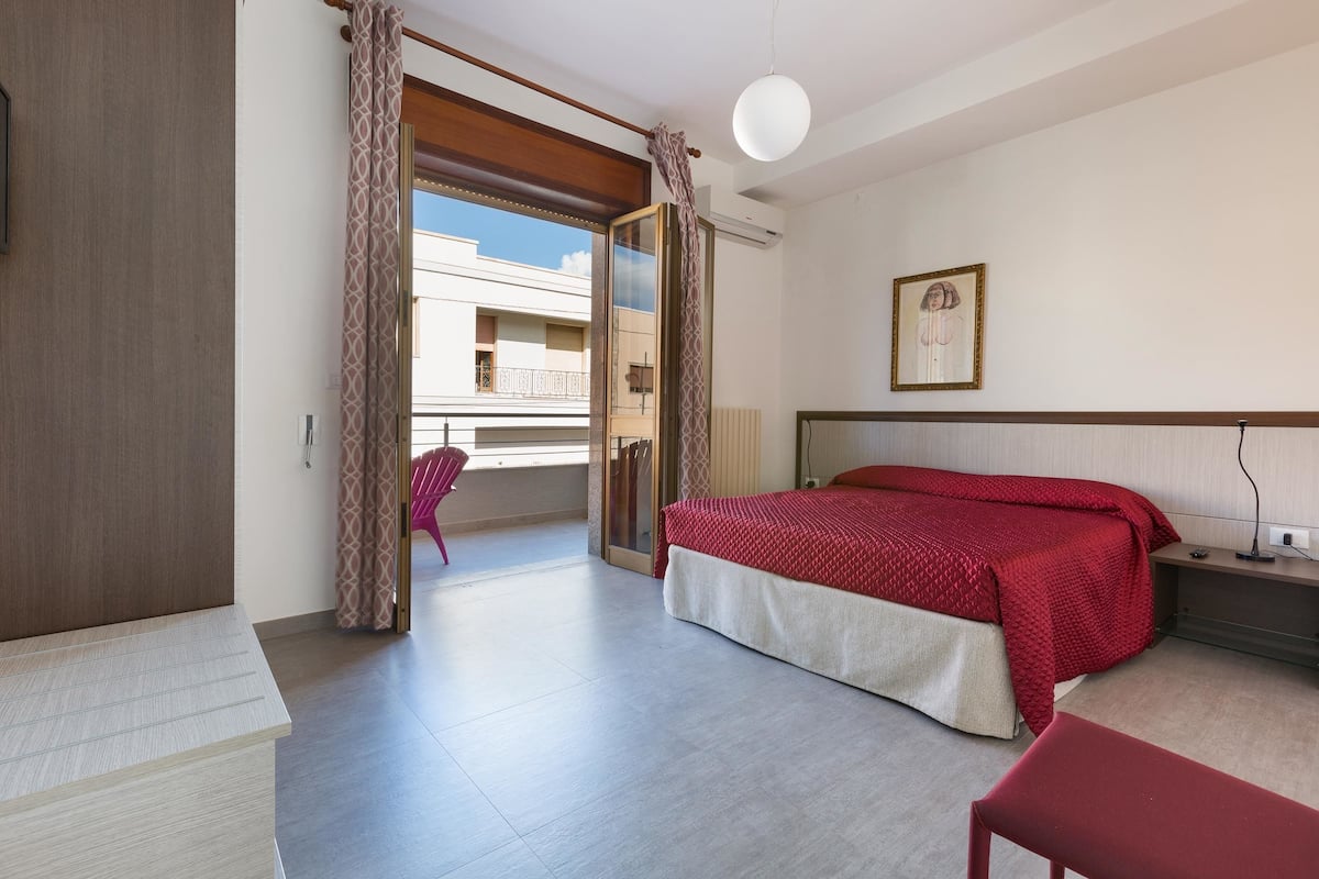 A hotel room with a bed, a desk, a chair, and a balcony with a view.