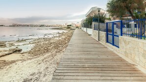 A wooden boardwalk along a beach with a stone wall and blue railing on one side. - Villa Syrmata (Porto Cesareo)
