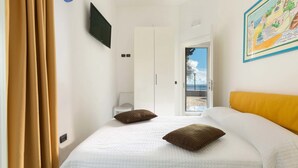 A hotel room with a bed, a TV mounted on the wall, a painting, and a view of the outside. - Villa Syrmata (Porto Cesareo)