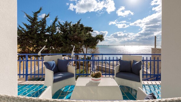 A balcony with wicker furniture, a small table, and a view of the sea. - Villa Syrmata (Porto Cesareo)