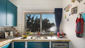A kitchen with blue cabinets, a double sink, and a window with a view of trees. - Villa Syrmata (Porto Cesareo)