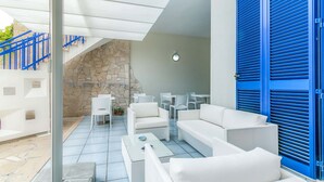 A modern outdoor living area with white furniture, a stone wall, and blue shutters. - Villa Syrmata (Porto Cesareo)