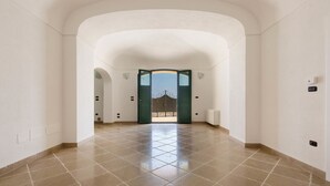 A spacious hallway with a tiled floor and white walls, leading to a door with a decorative metal gate. - Villa Dorella (Castrignano del Capo)