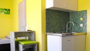 Eine kleine Küche mit grüner Fliesenrückwand, Spüle und einem kleinen Holzhocker.