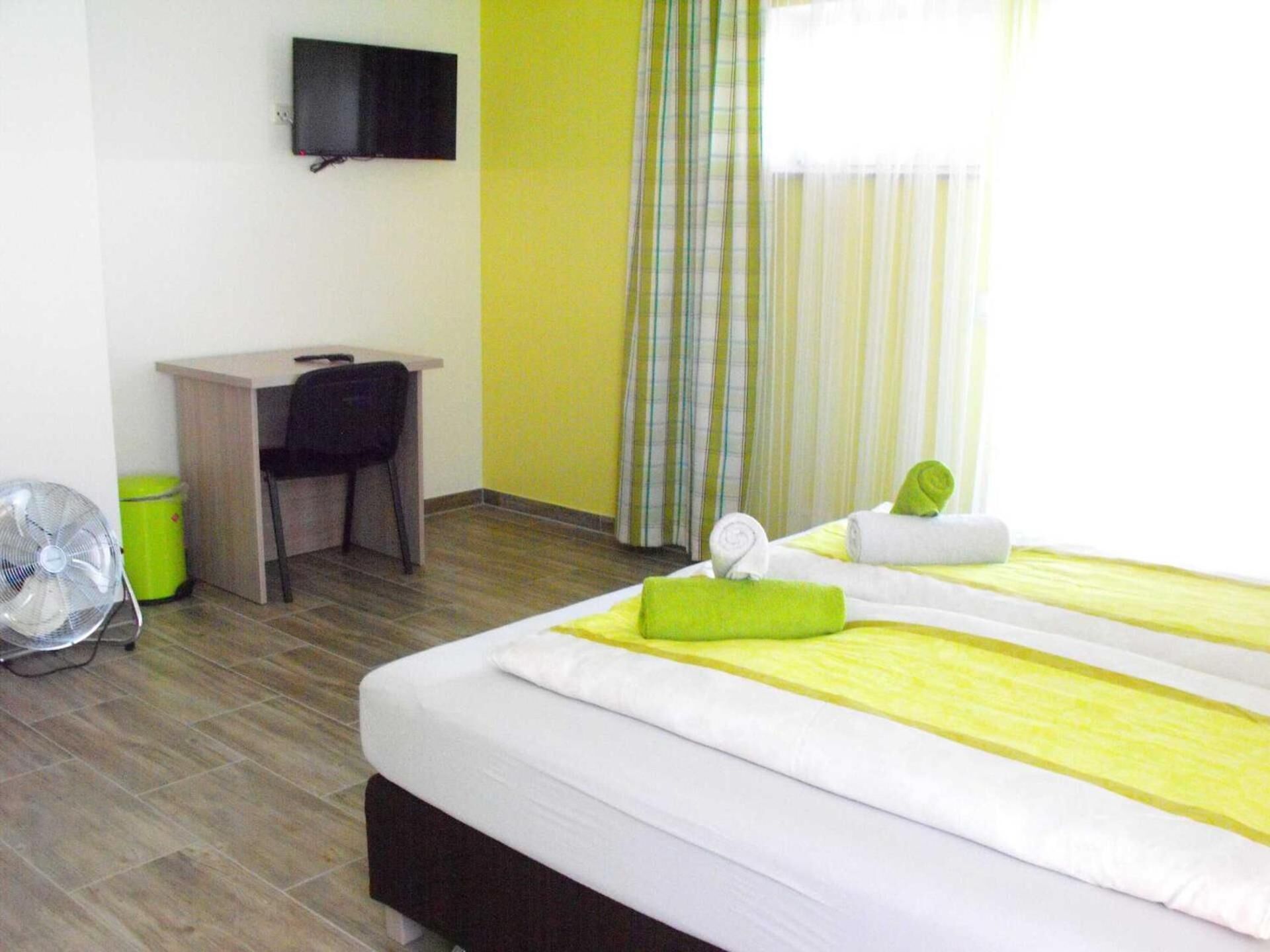 A hotel room with a bed, a desk, a chair, a TV, and a window with curtains.
