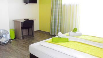 A hotel room with a bed, a desk, a chair, a TV, and a window with curtains.