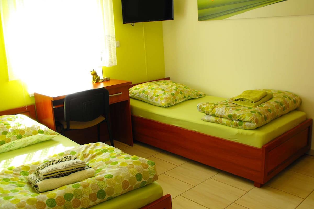 Une chambre avec deux lits simples, un bureau, une chaise, une télévision et une fenêtre avec des rideaux.