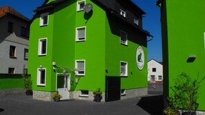 Ein grünes Gebäude mit mehreren Fenstern und einer Tür, umgeben von anderen Bauten.