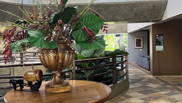 A lobby with a large decorative vase on a wooden table, a modern ceiling, and a sign indicating room numbers.