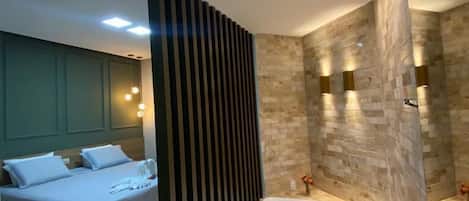 A modern hotel room with a large bed, a separate bathroom with a bathtub, and a glass-enclosed shower area.