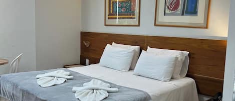 A hotel room with a bed, bedside table, and two framed artworks on the wall.