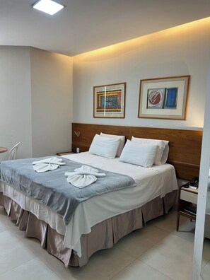 Ein Hotelzimmer mit einem Bett, einem Nachttisch und zwei gerahmten Kunstwerken an der Wand.