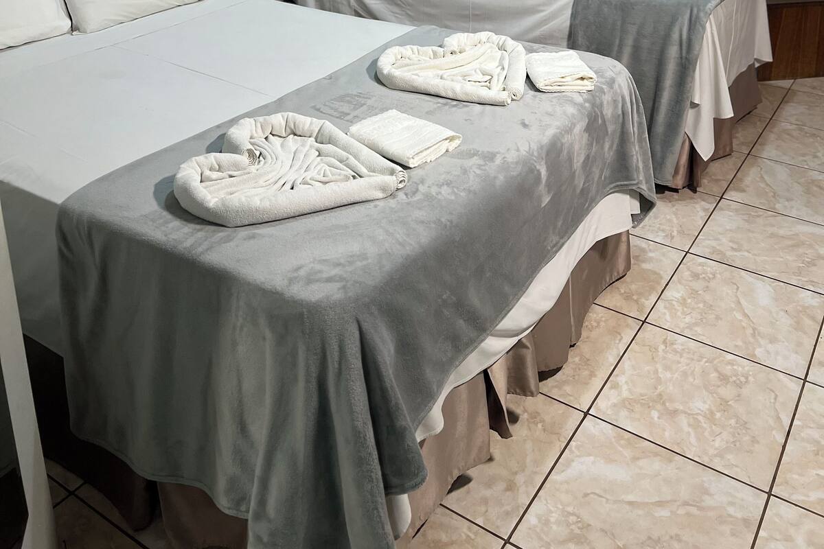 Une chambre d’hôtel avec deux lits, des couvre-lits gris, des oreillers blancs et des serviettes sur les lits. Deux œuvres d’art encadrées sont accrochées au mur.