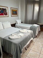 Quarto de hotel com duas camas, colchas cinzentas, almofadas brancas e toalhas sobre as camas. Existem duas obras de arte emolduradas na parede.