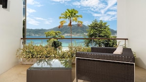 A balcony with a glass-top table, wicker furniture, and a view of a mountain and sea. - Atika Villa 1 oceanfront pool villa (Patong)