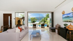 A modern living room with a sofa, coffee table, and a view of a pool and mountains. - Atika Villa 1 oceanfront pool villa (Patong)