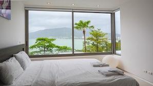 A bedroom with a large window, a bed, and a view of a body of water and trees. - Atika Villa 1 oceanfront pool villa (Patong)