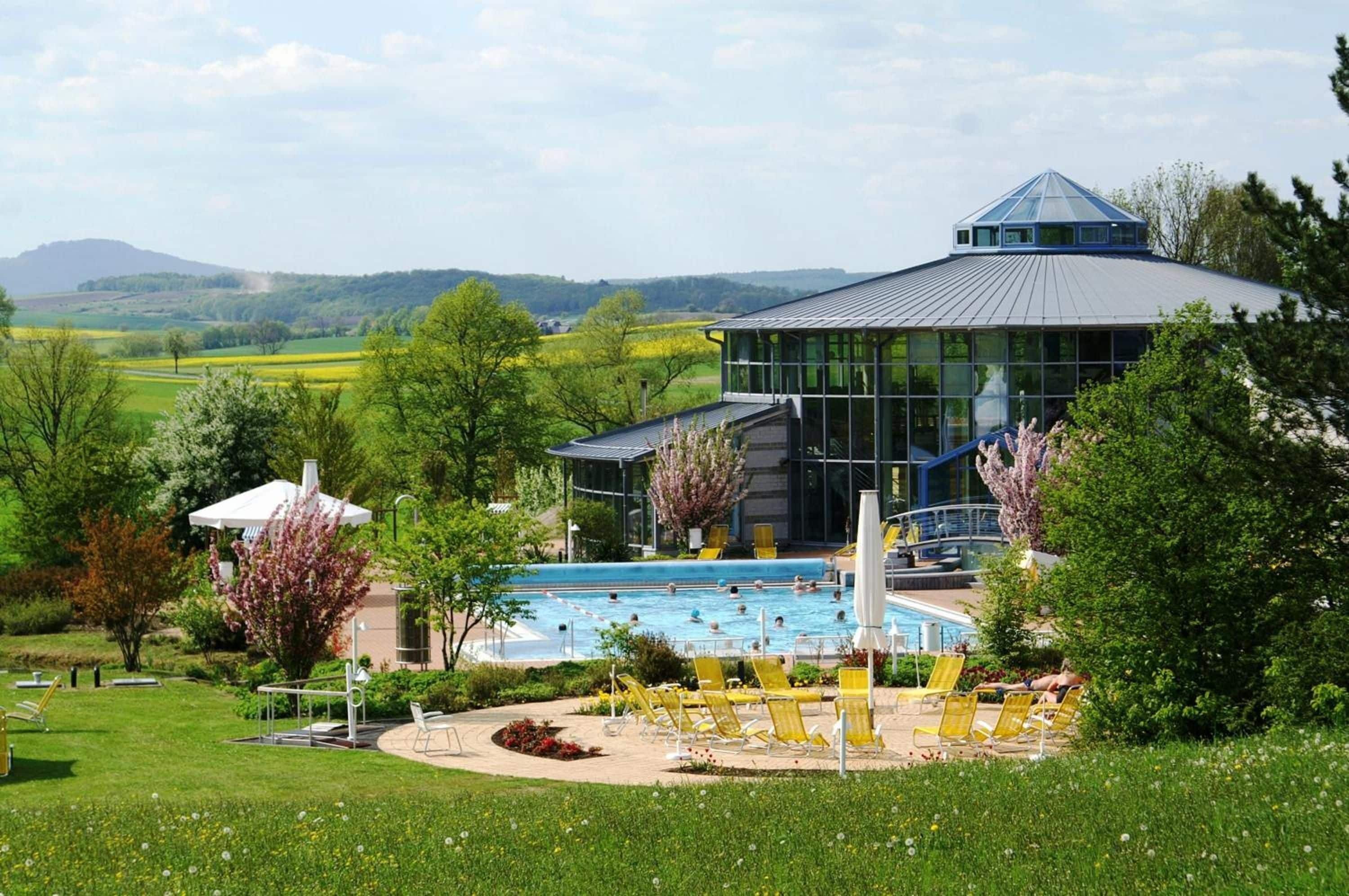 A modern building with a swimming pool, surrounded by lush greenery and a view of rolling hills.