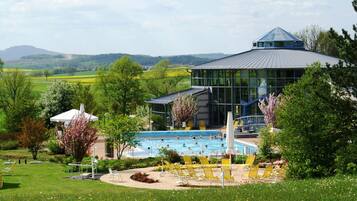 A modern building with a swimming pool, surrounded by lush greenery and a view of rolling hills.