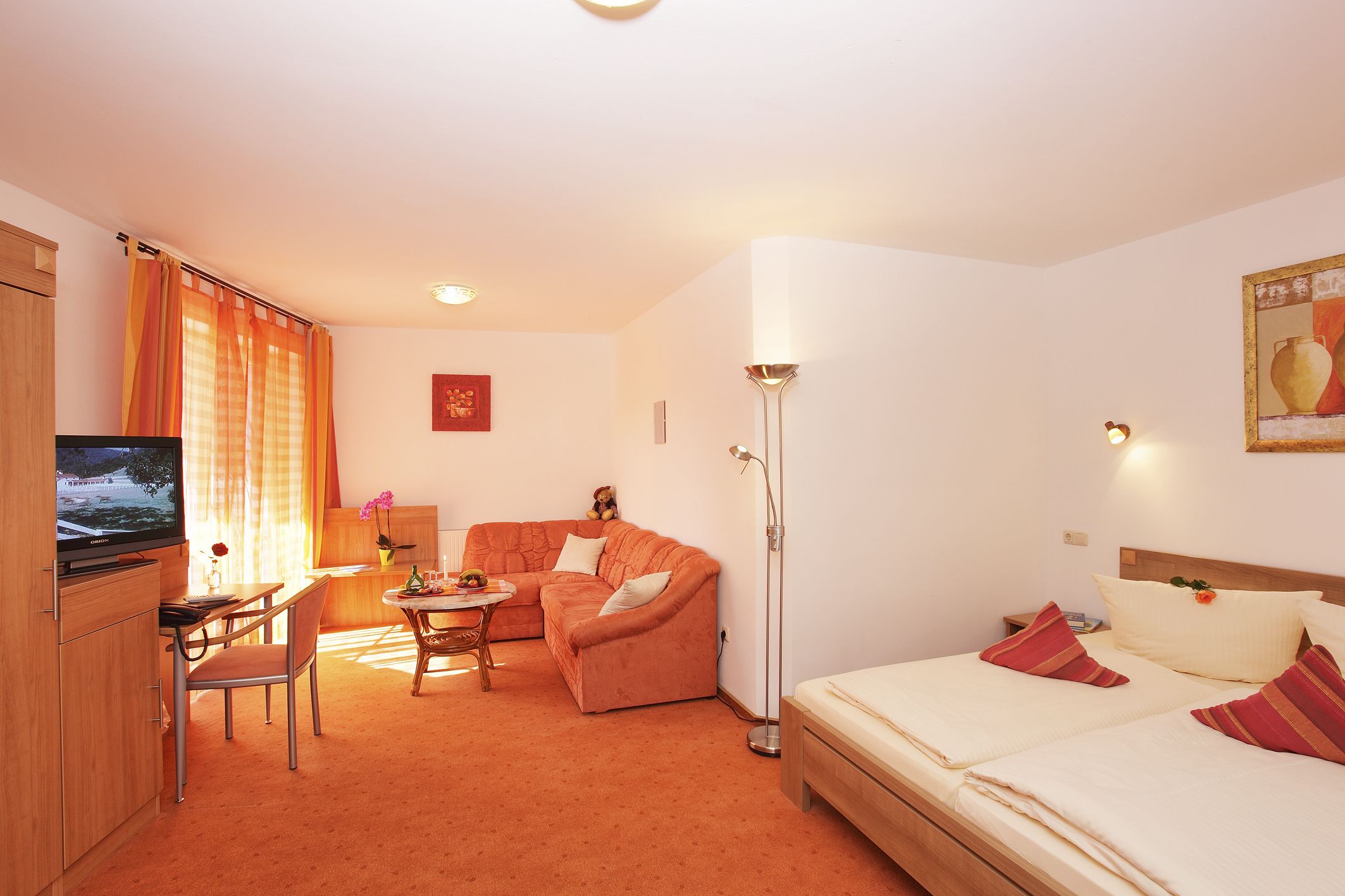 Habitación de hotel con cama, sofá, escritorio con silla, televisión y lámpara de pie.