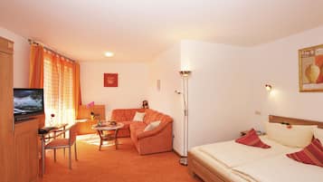 Habitación de hotel con cama, sofá, escritorio con silla, televisión y lámpara de pie.
