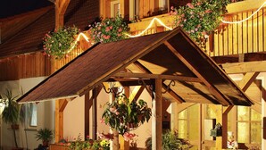 Un bâtiment rustique en bois, agrémenté d’une fontaine en pierre, de plantes en pot et de guirlandes lumineuses.