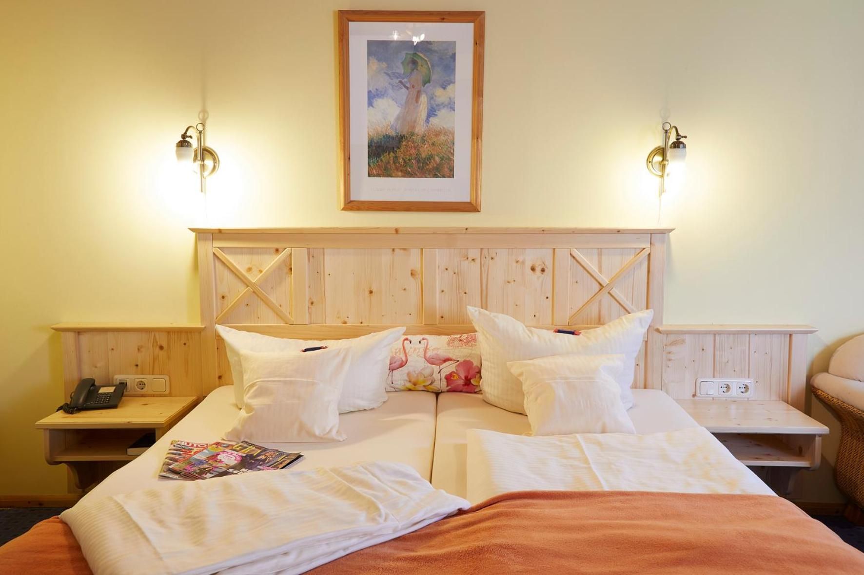 Una cama doble con cabecera de madera, dos mesitas de noche, un teléfono y un cuadro enmarcado en la pared.